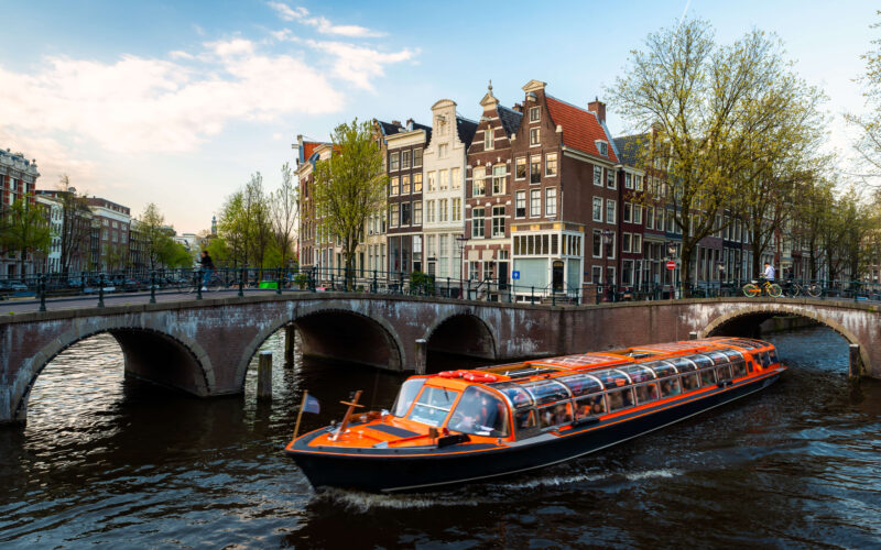 Orange canal cruise boat passing under a bridge on the Amsterdam canals — things to do from the cruise port