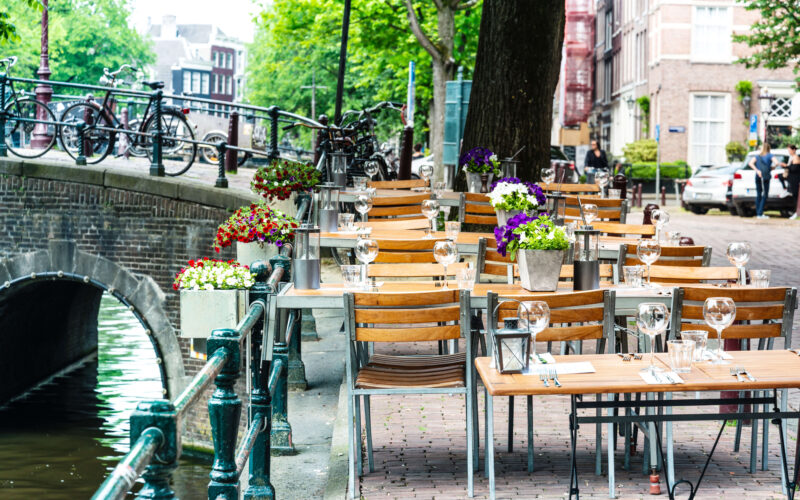 Canal-side restaurant terrace in Amsterdam with flower-decorated tables and bicycles on the bridge — where to eat near the cruise port