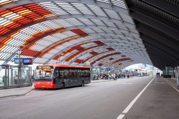 R-NET bus at Amsterdam Centraal station bus terminal under the curved architectural roof, connecting IJmuiden cruise port to Amsterdam city centre