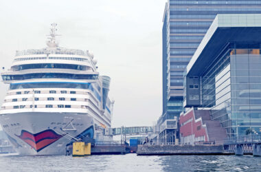 Cruise ship docked at the Passenger Terminal Amsterdam (PTA) on the IJ waterfront, with the modern terminal building alongside