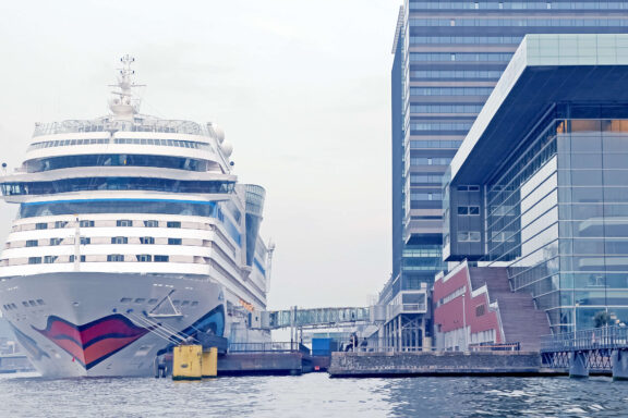 Cruise ship docked at the Passenger Terminal Amsterdam (PTA) on the IJ waterfront, with the modern terminal building alongside