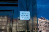 Anne Frank Huis nameplate on the entrance door at Prinsengracht 263, Amsterdam, with canal houses reflected in the door