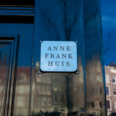 Anne Frank Huis nameplate on the entrance door at Prinsengracht 263, Amsterdam, with canal houses reflected in the door