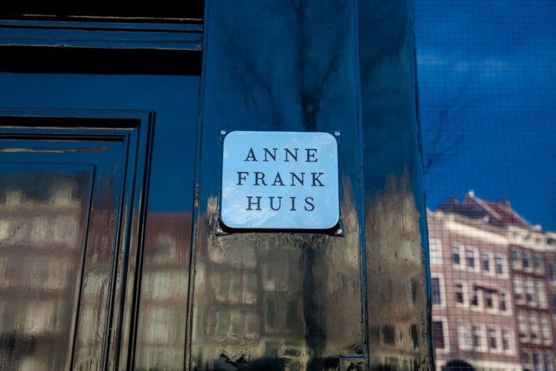 Anne Frank Huis nameplate on the entrance door at Prinsengracht 263, Amsterdam, with canal houses reflected in the door