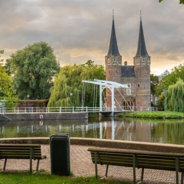 The medieval Oostpoort city gate with white drawbridge reflected in the canal, Delft, Netherlands — a popular day trip from Dutch cruise ports