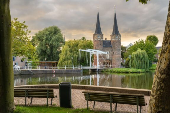 The medieval Oostpoort city gate with white drawbridge reflected in the canal, Delft, Netherlands — a popular day trip from Dutch cruise ports