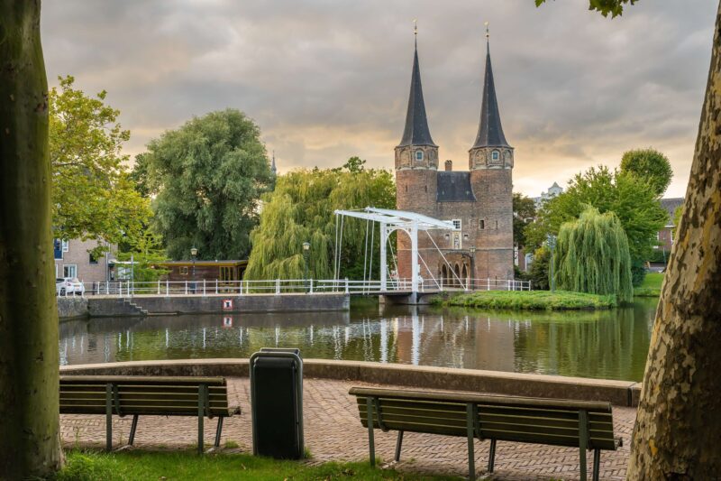 The medieval Oostpoort city gate with white drawbridge reflected in the canal, Delft, Netherlands — a popular day trip from Dutch cruise ports