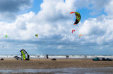 Kitesurfers on the wide sandy beach at IJmuiden with colourful kites in the sky and North Sea waves in the background