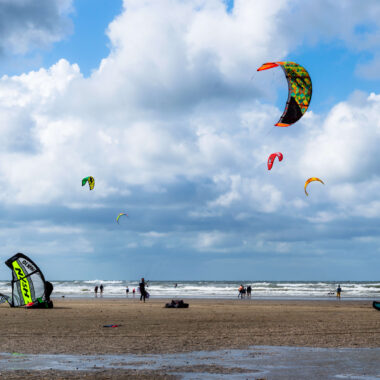 Kitesurfers on the wide sandy beach at IJmuiden with colourful kites in the sky and North Sea waves in the background