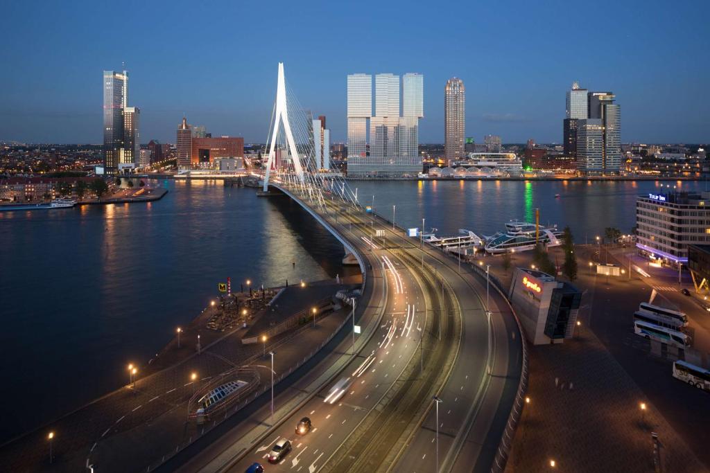The Erasmus Bridge and the Wilhelminapier skyline at dusk, with traffic light trails on the road below