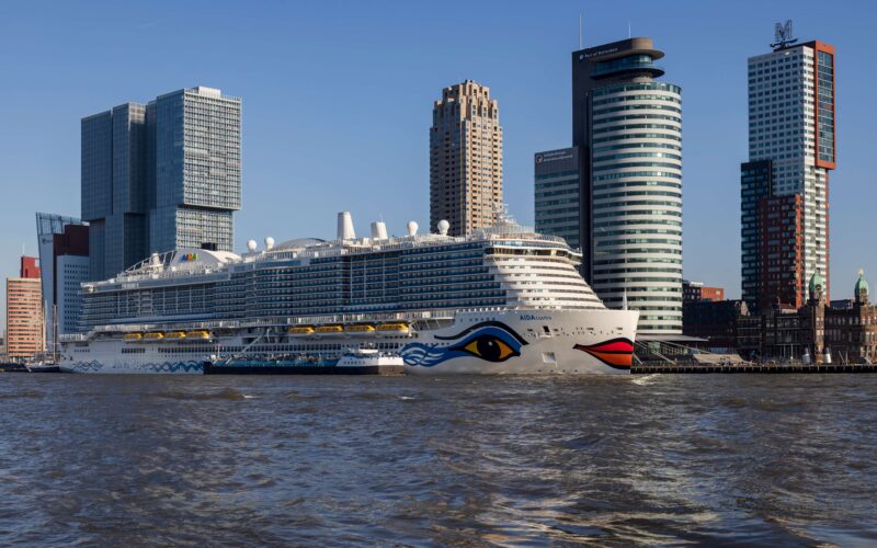 AIDACosma cruise ship docked at Rotterdam Cruise Terminal on Wilhelminapier, with the Rotterdam city skyline and Port of Rotterdam tower in the background