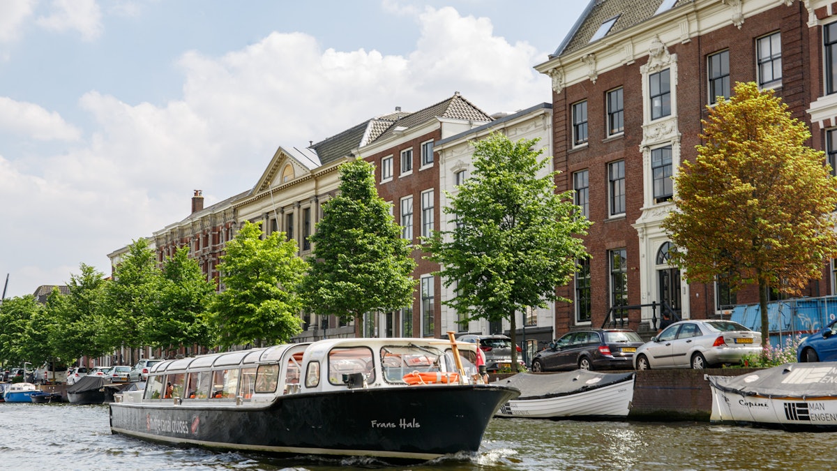 A canal boat moored on a tree-lined Haarlem canal in front of tall brick houses