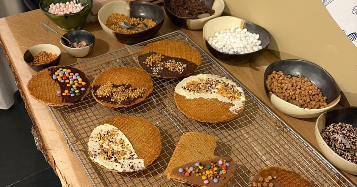 Freshly baked stroopwafels cooling on a rack surrounded by bowls of toppings