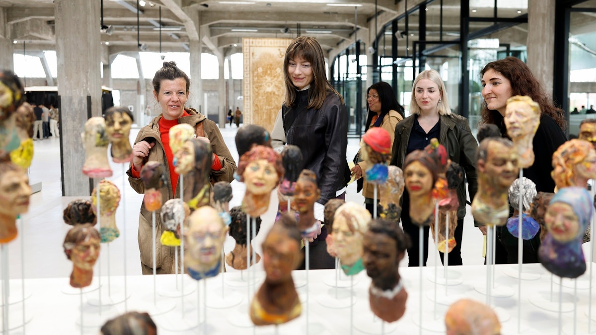 Visitors at the Fenix museum looking at an installation of sculpted heads inside the converted warehouse