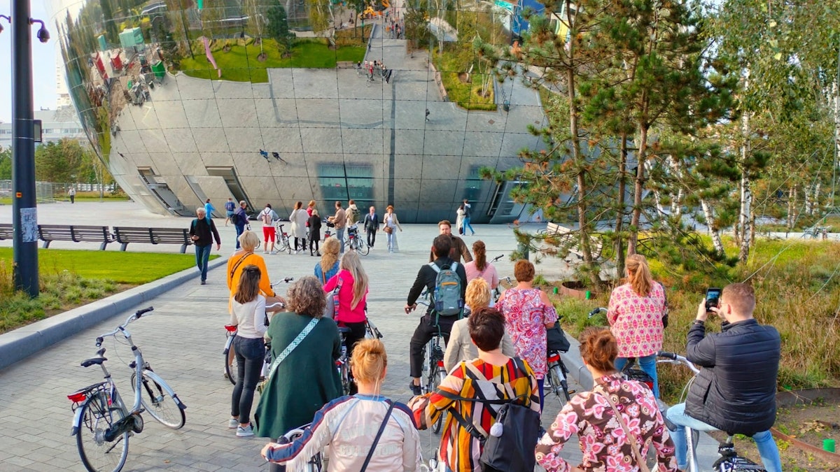A guided bike tour group pausing with their bikes in a green Rotterdam city space